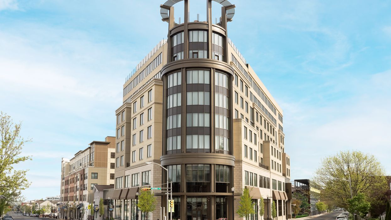 Exterior view of the modern eight-story MC Hotel in Montclair, NJ, with a curved glass facade and rooftop structure, located in a vibrant downtown area, 2025