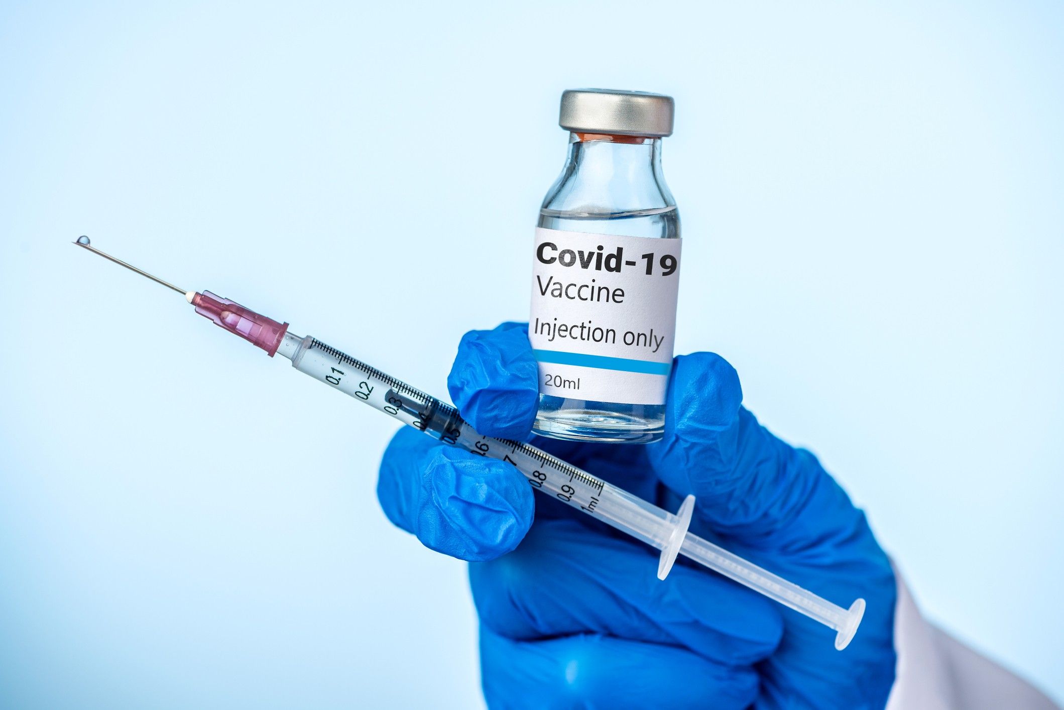 Doctor or nurse is holding the Covid-19 vaccine and syringe with her blue glove.