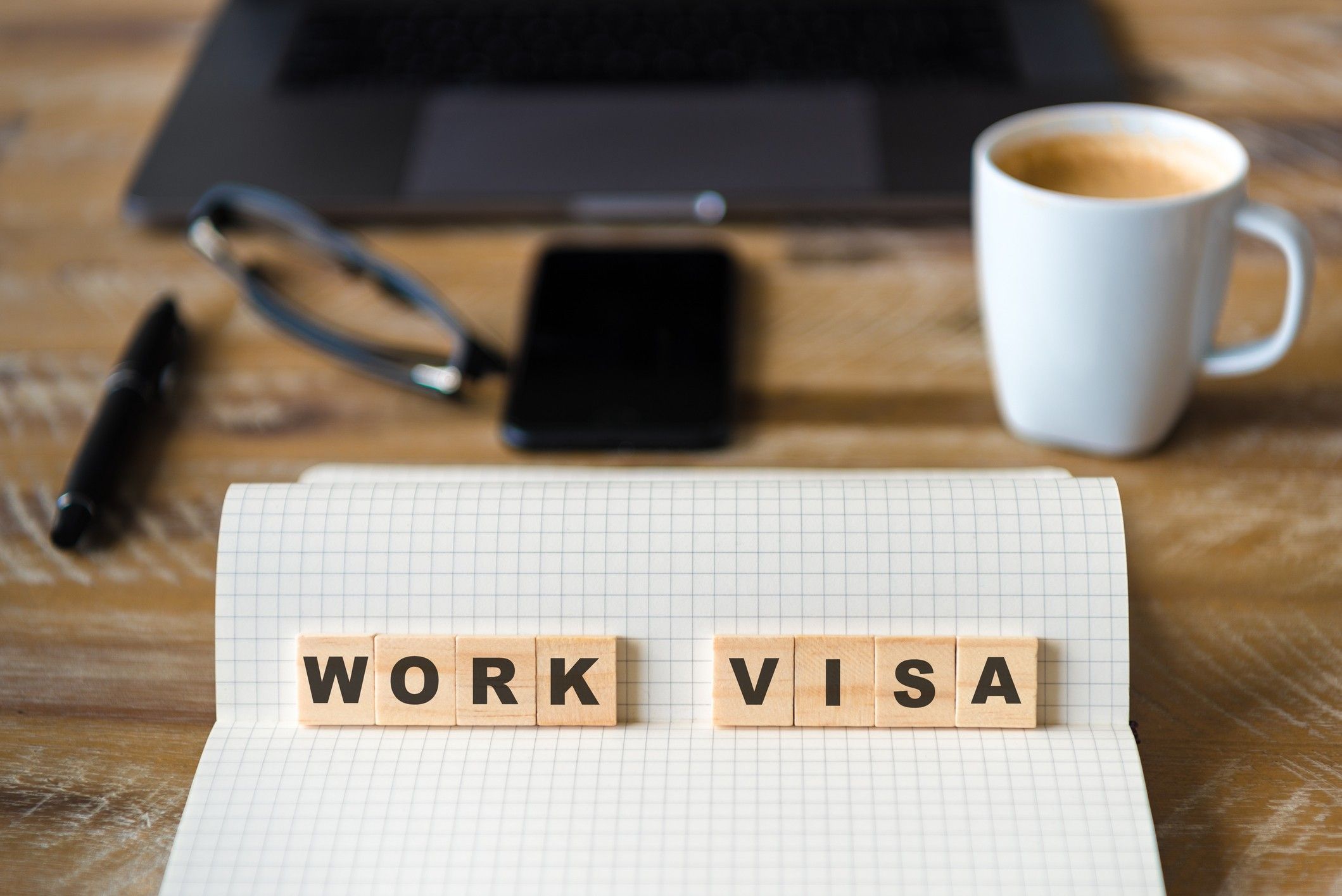 Closeup on notebook over wood table background, focus on wooden blocks with letters making Work Visa text